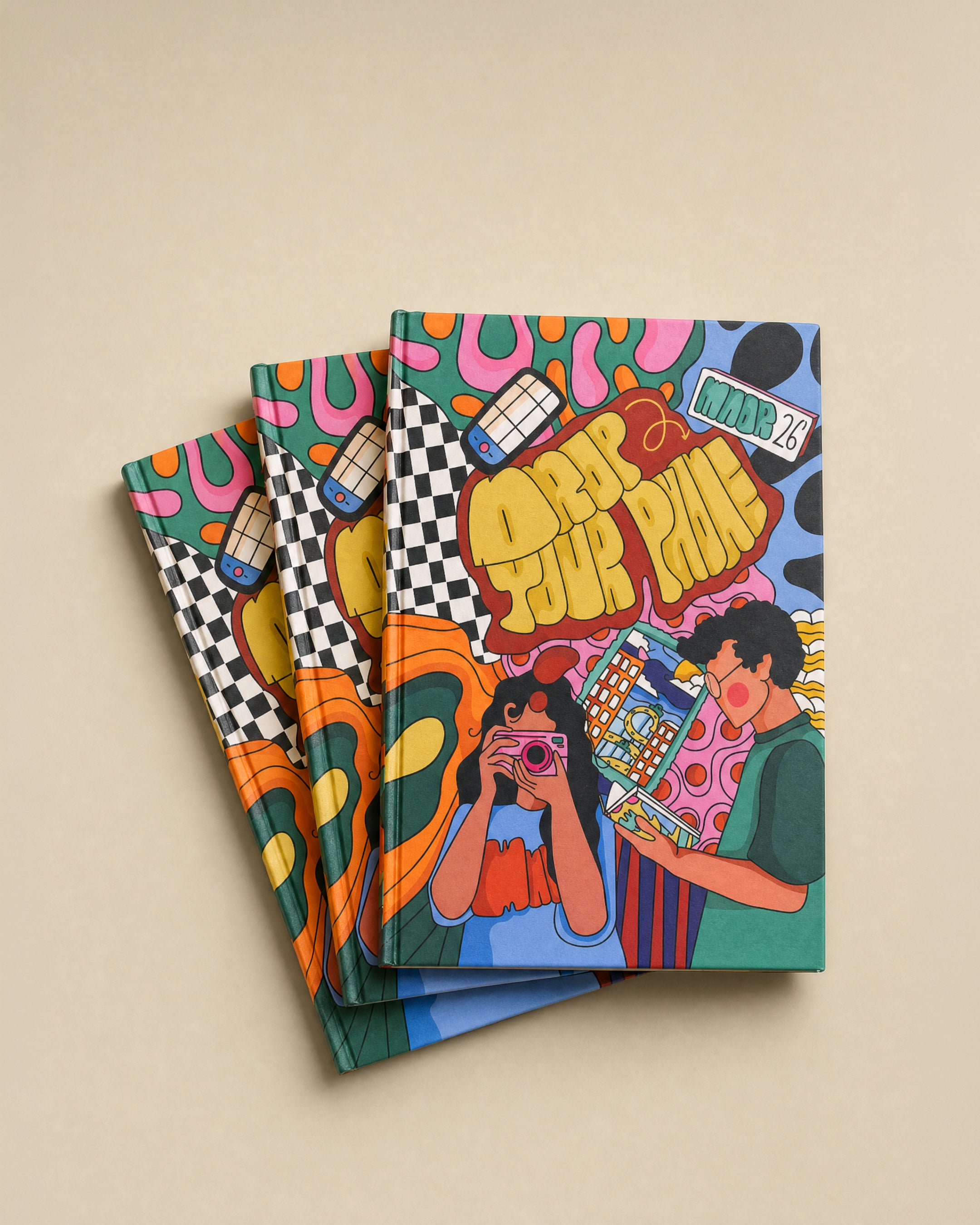 Three colorful illustrated notebooks or journals stacked slightly offset on a plain beige background. The cover art features a playful doodle-style design with the text 'DROP YOUR PHONE' and a cartoon character holding a camera, with additional abstract shapes and patterns in pink, yellow, green, blue, orange, black, and white.
