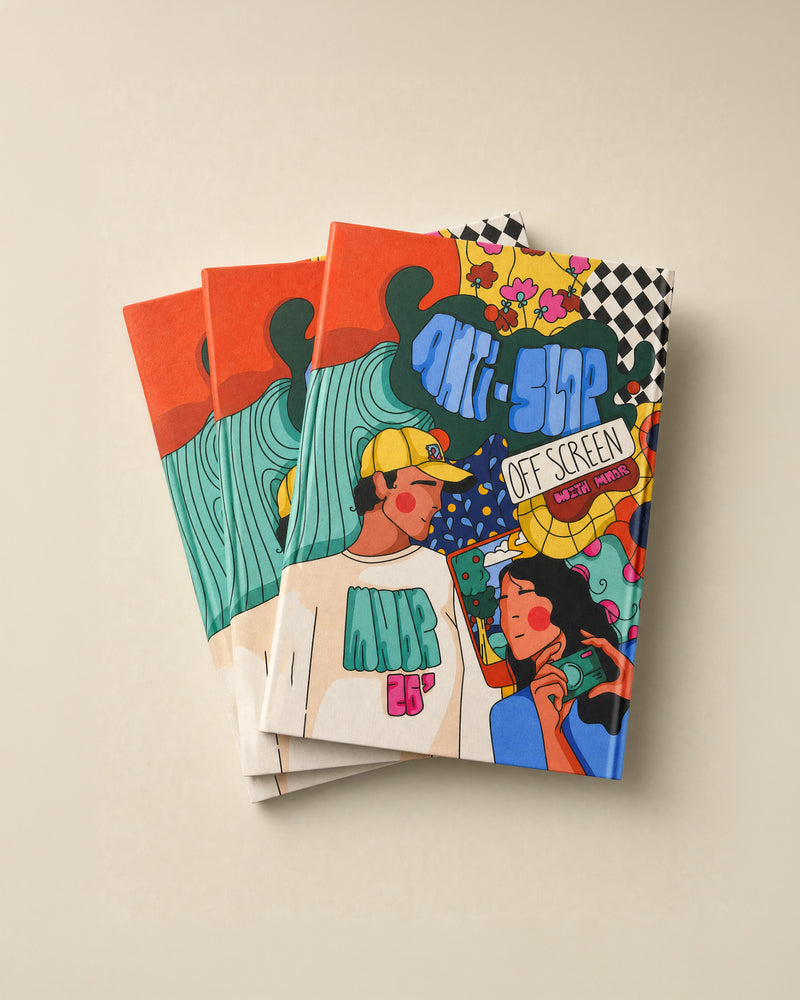 Three stacked notebooks/photobooks with colorful illustrated covers on a light beige background. The covers feature vibrant doodle-style art with text including 'ANTI-SLOP', 'OFF SCREEN', and 'WITH MNDR'.